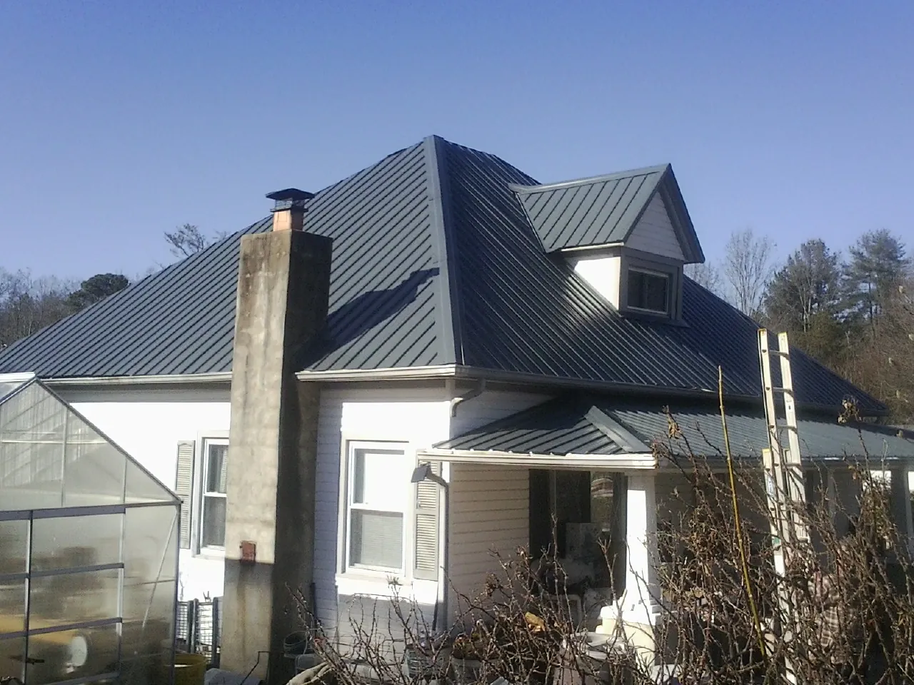 Dark blue standing seam metal roof on a white farmhouse with dormer — Slate & Tile Roof Repair by Roofing Brothers in Harbor Springs