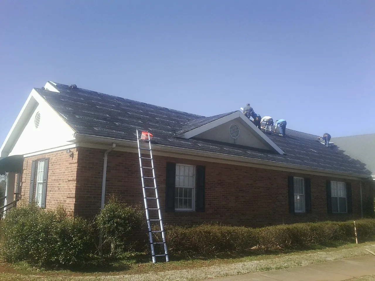 Crew tearing shingles off a brick ranch roof with a ladder set — Metal Roof Repair work by our crew in Harbor Springs
