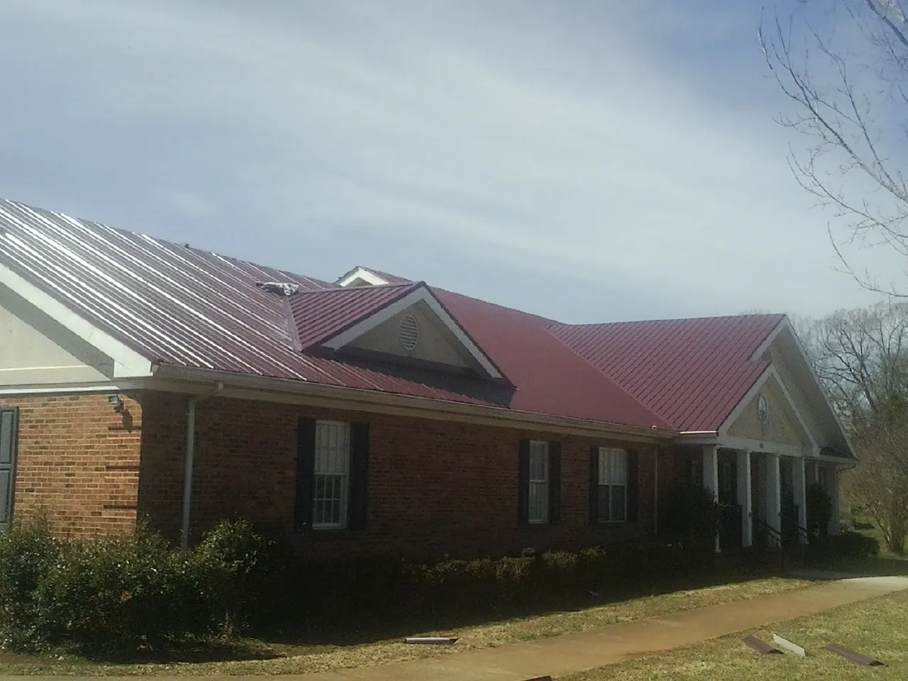 Red metal roof with gabled entries on a long brick building, from a Hail Damage Roof Repair job in Harbor Springs