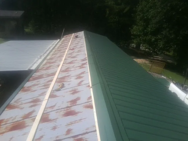 Old rusted panels beside newly installed green metal roofing — Wind Damage Roof Repair by Roofing Brothers in Harbor Springs
