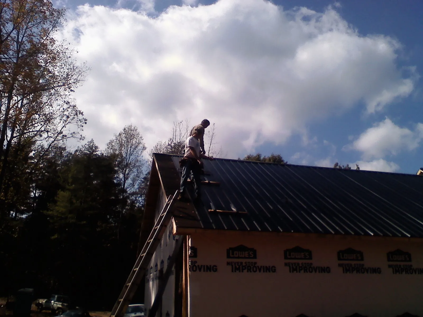 Roofer fastening dark metal panels high against a cloudy sky, from a Roof Inspection job in Harbor Springs