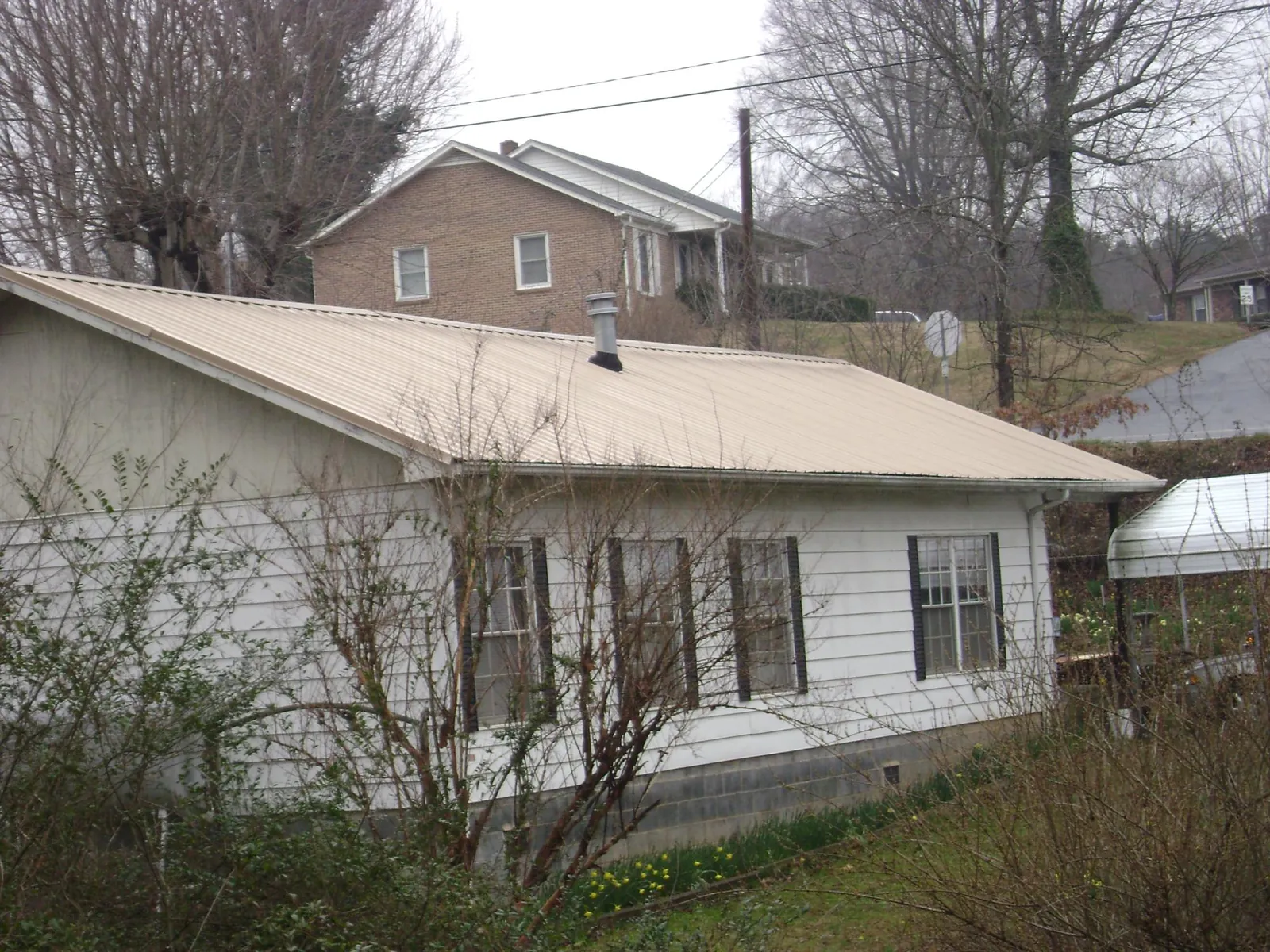 Tan metal roof on a white sided house set into a hillside — Commercial Roofing by Roofing Brothers in Harbor Springs
