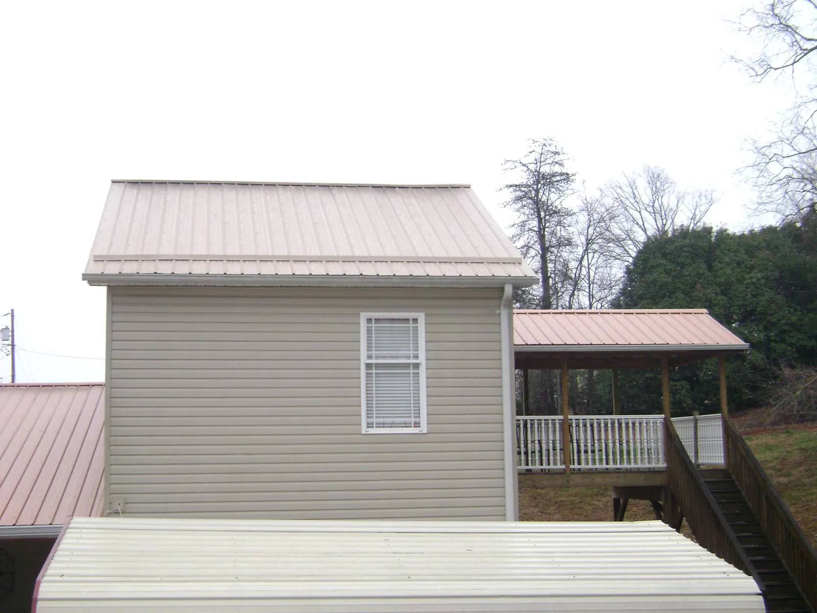 Tan metal roofs on a two story addition and attached porch, from a Roof Replacement job in Harbor Springs