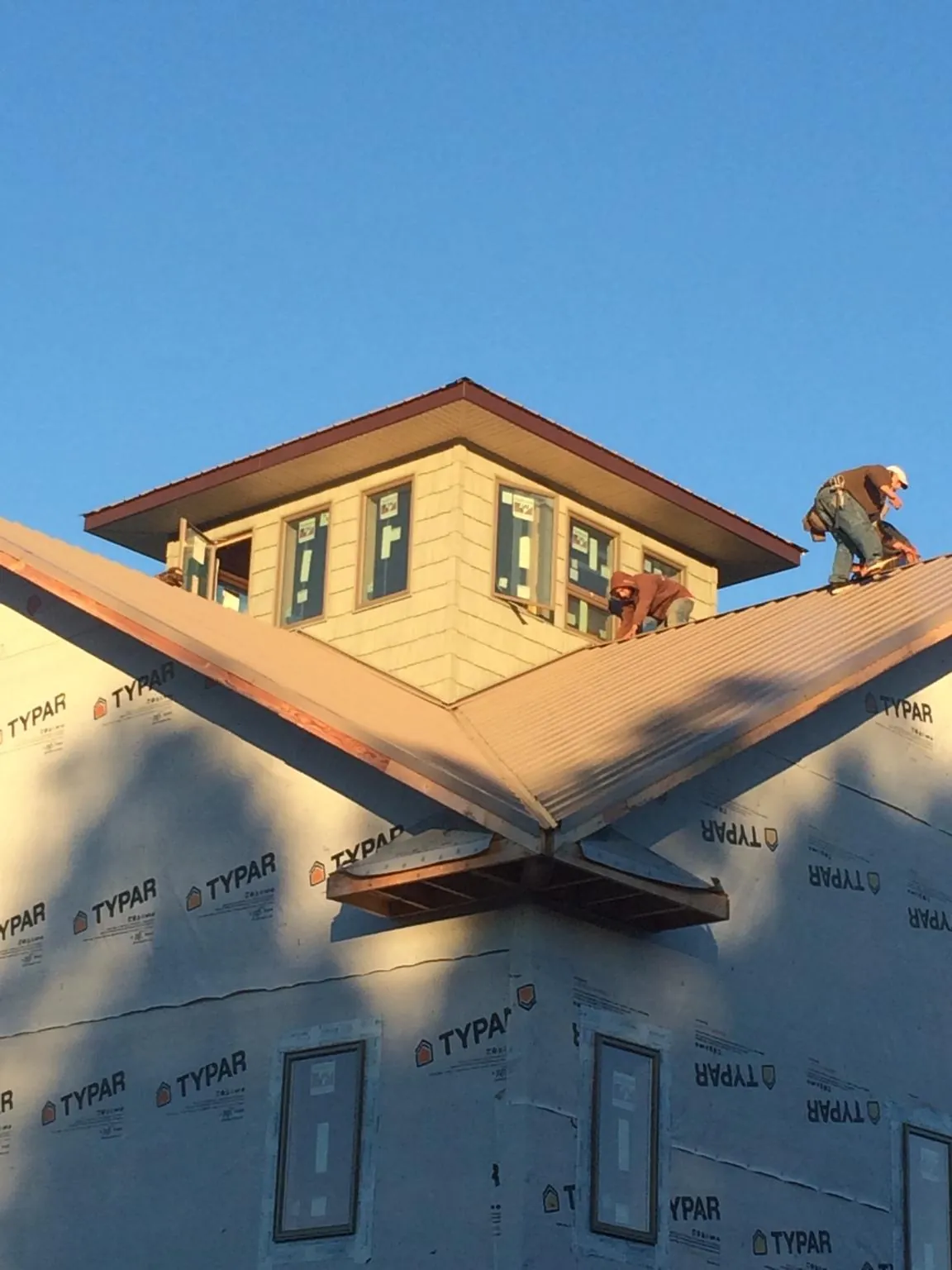 Roofers working around a rooftop cupola on a new metal roof at sunset — Roof Waterproofing in Harbor Springs by Roofing Brothers